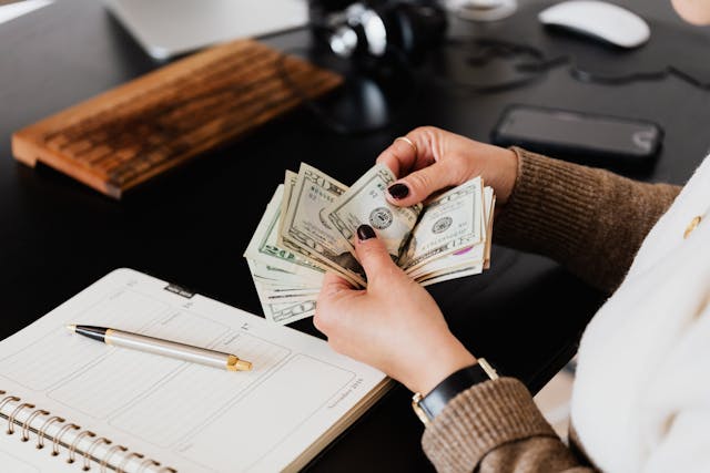 Person counting money with a notepad and a pen in the background